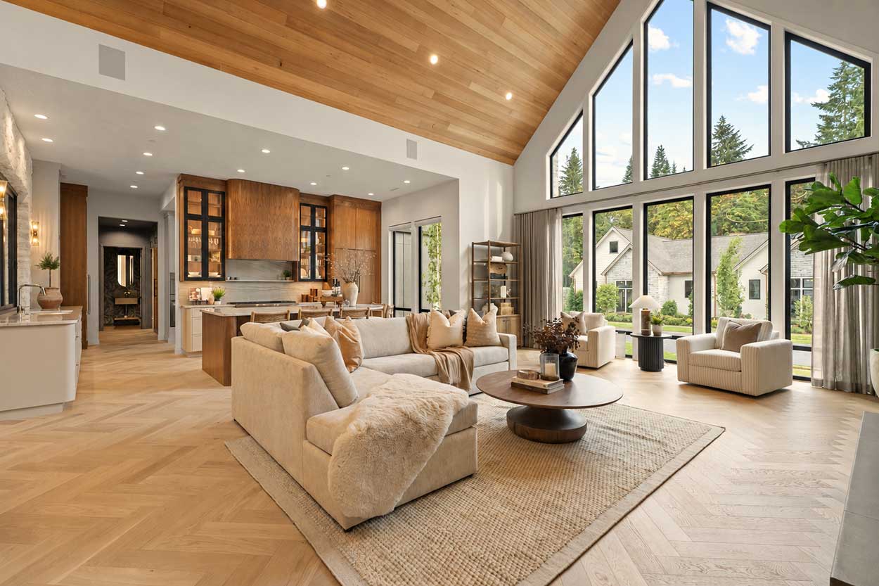 Great room with soaring gabled windows, cream sectional and swivel chairs, round wood coffee table, and open kitchen beyond.