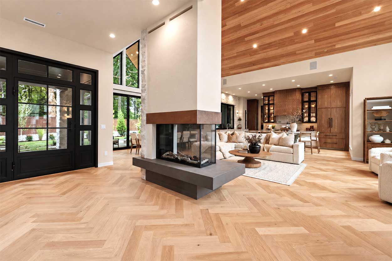 Open living area with black steel-framed entry doors, a three-sided fireplace, herringbone oak floors, and a walnut kitchen beyond.