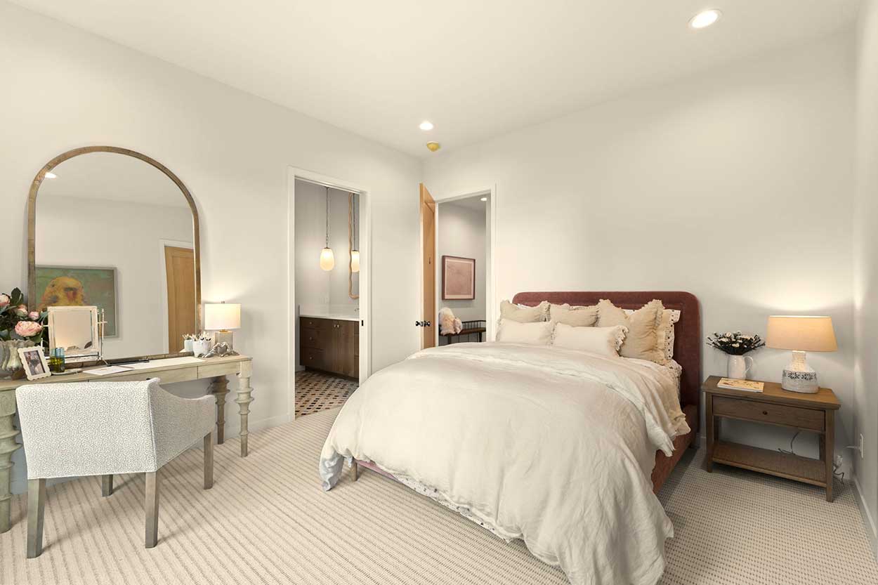 Bedroom with a rose velvet headboard, arched floor mirror, carved vanity desk, and a view into the ensuite bath.